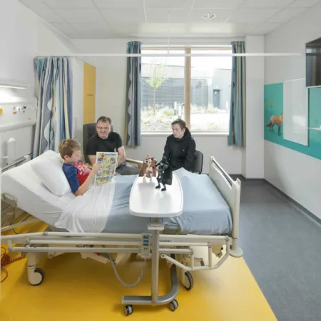 Private room at the Royal Hospital for Sick children and Young People, Edinburgh. A boy is in bed with receiving visitors in this bright hospital room. Colour and illustration is used on the floor and walls.