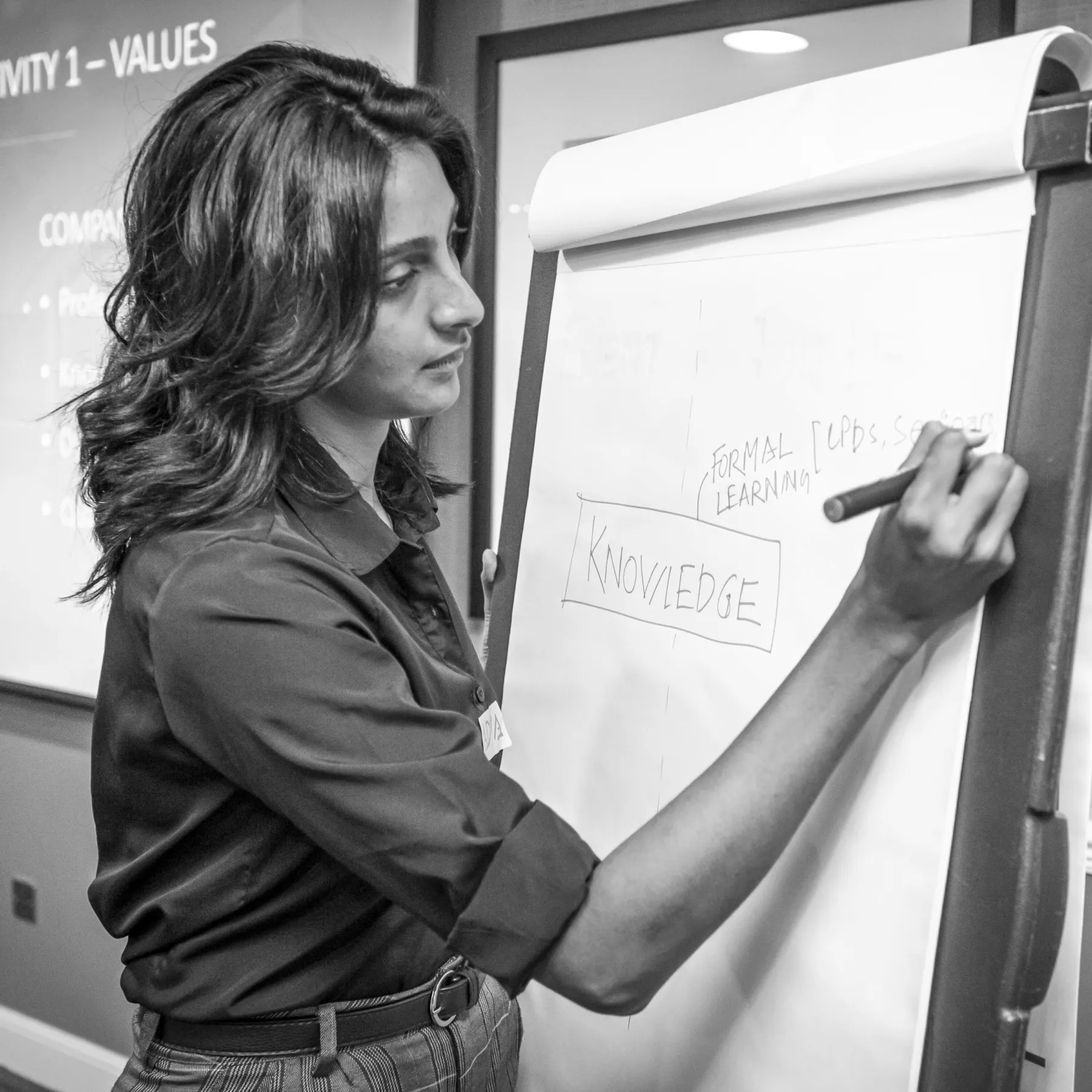 A young, female construction consultant writes on a flip chart during a Thomson Gray Construction Consultants event. She holds a marker in her right hand and draws a mind map with "knowledge" at the centre.