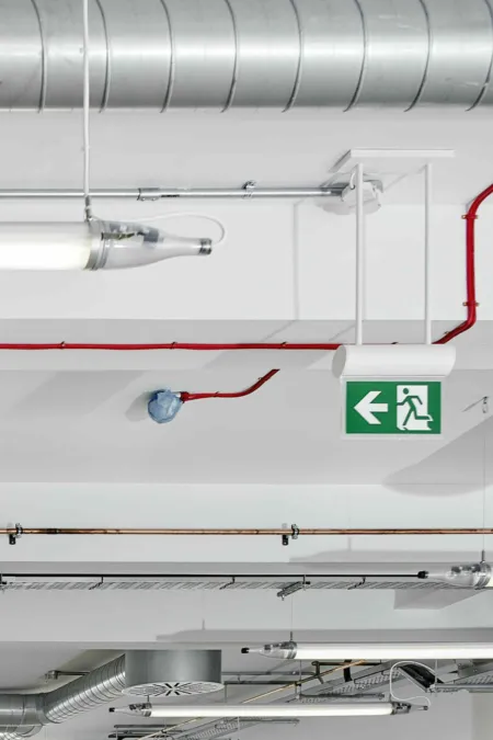 Detail of exposed services and wiring showing escape signs  and fire alarm.