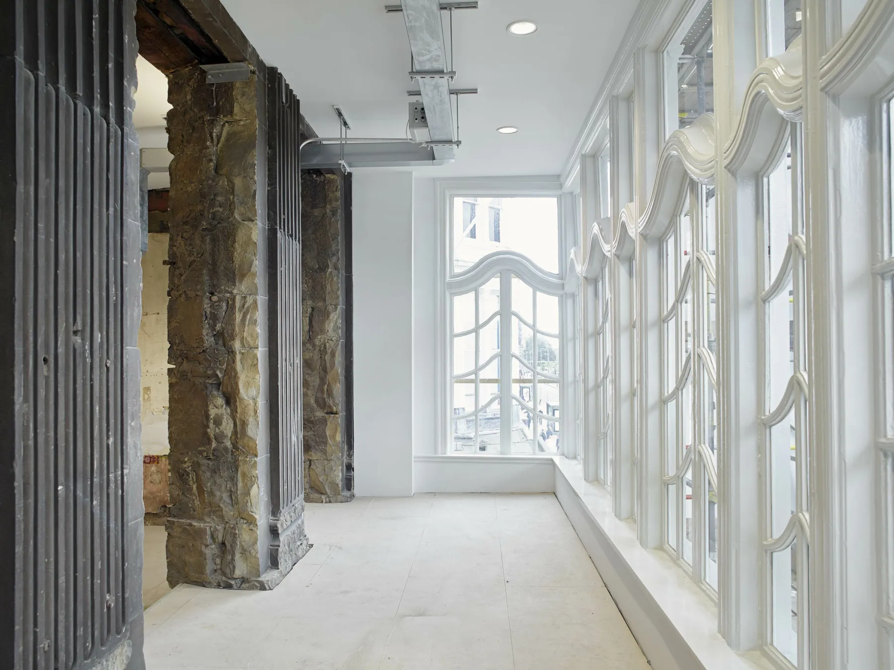 Interior view of defurbished office in listed building, Edinburgh. Exposed stone contrasts with complex, timber window frames.