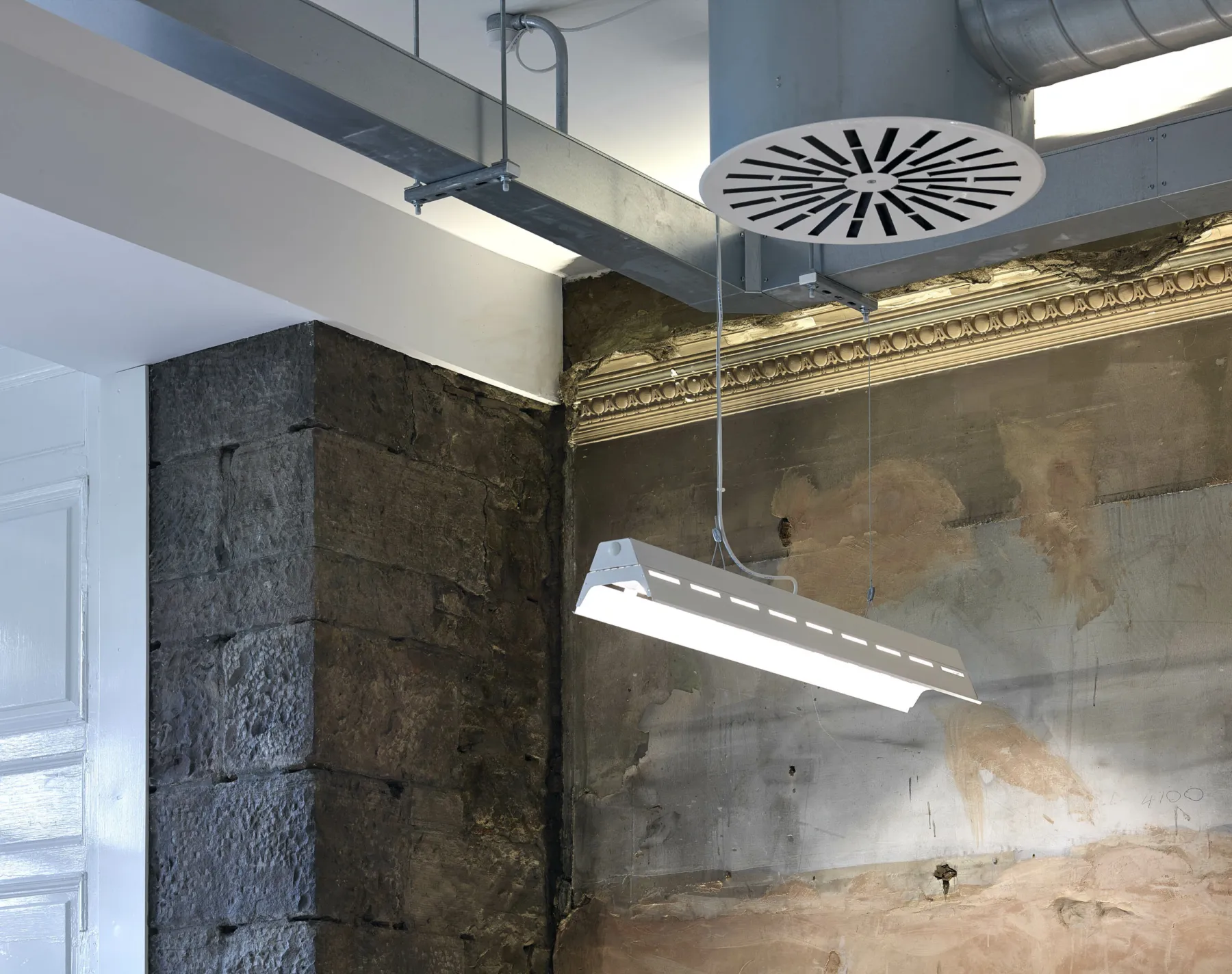 Detail of a listed building on Princes Street, Edinburgh used for offices. Exposed stone and cornicing is shown alongside galvanised steel ducting and vents. Pendant lighting illuminates the exposed plaster wall.