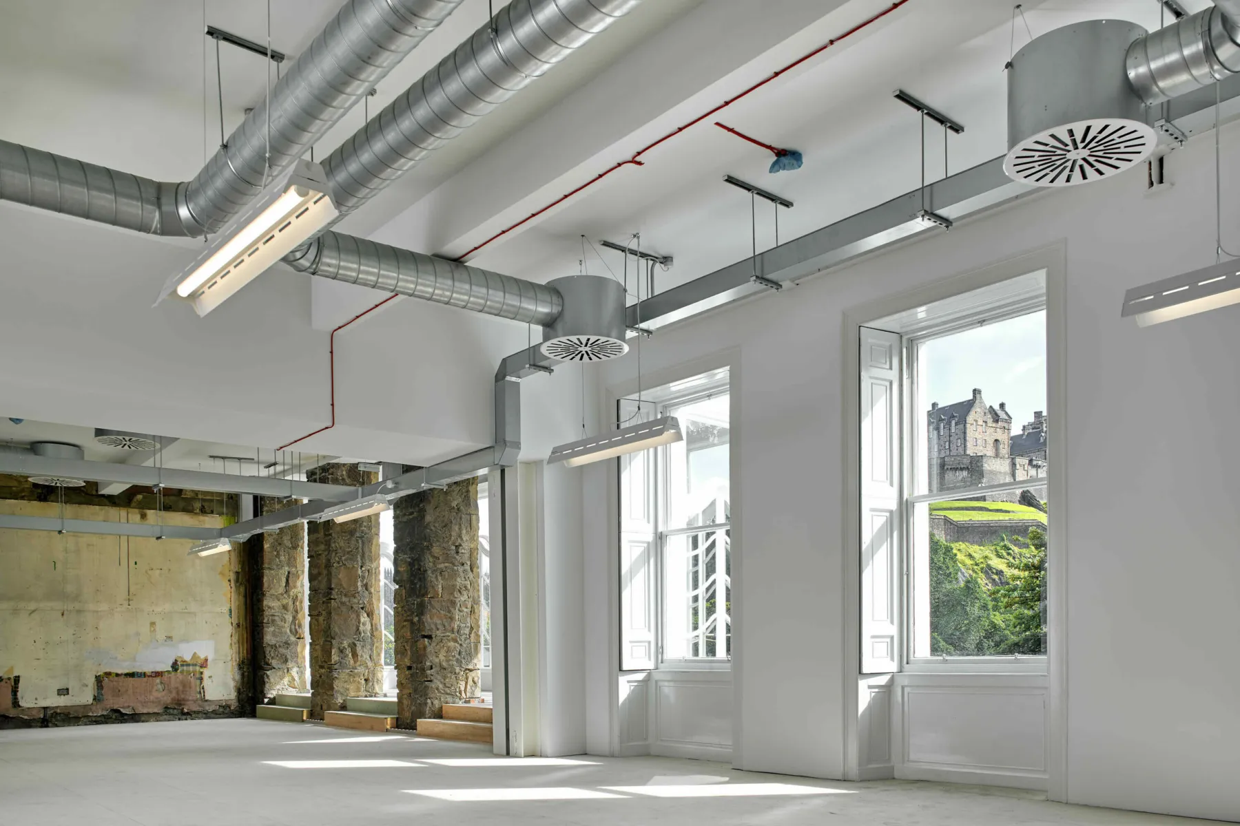 Inside a refurbished listed building on Princes St Edinburgh. Exposed stone work and ducting is contrasted with cornicing and panelling. The space has been restored to be used as office accommodation. Through the window, a view to Edinburgh Castle.
