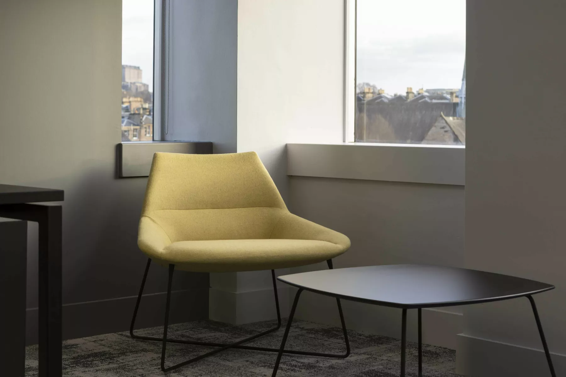 Detailed of relaxed seating area in Cat-B full office refurbishment, Edinburgh. Contempory, wire-framed armchair with yellow upholstery. Black, wire framed low table.