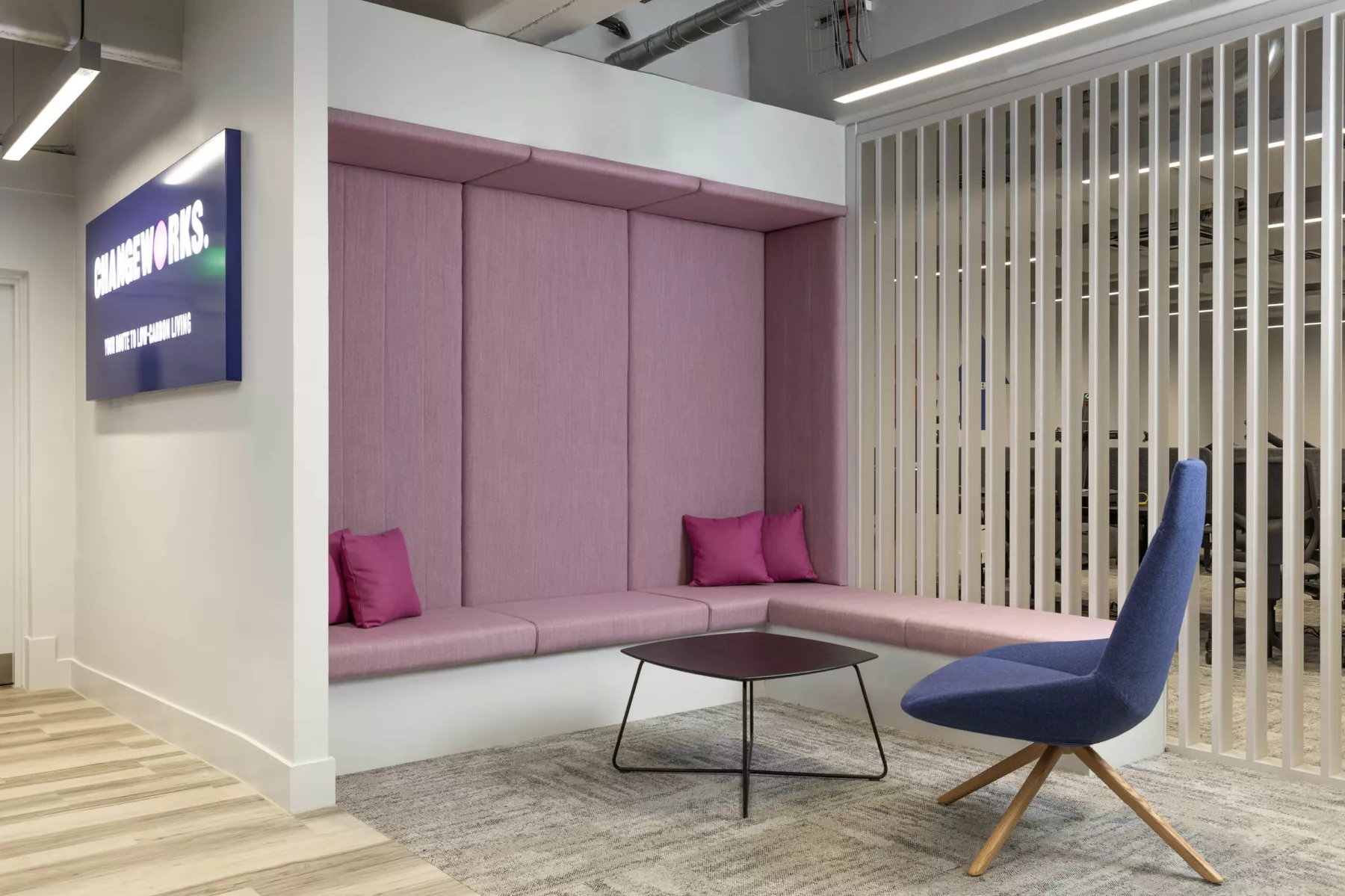 Group seating area with upholstery for sound insulation, and relaxed seating in the contemporary cat-B office fit out for Changeworks, Edinburgh. Recessed seating is upholstered in dusky pink. An easy chair in blue and a wire-framed table. Slatted, open partition. runs floor to ceiling.