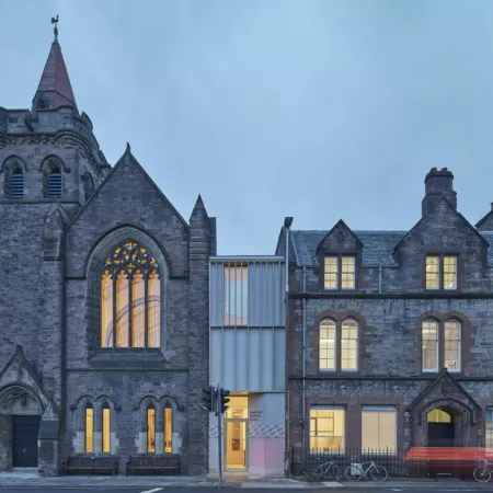Exterior view of the Greyfriars Charteris Centre after extensive conservation work to the historic church building, refurbishment and extension. Between the former church and sandstone offices there is now a contemporary extension in timber with terrazzo render. the photograph shows twighlight with traffic and people passing - blurred with motion.