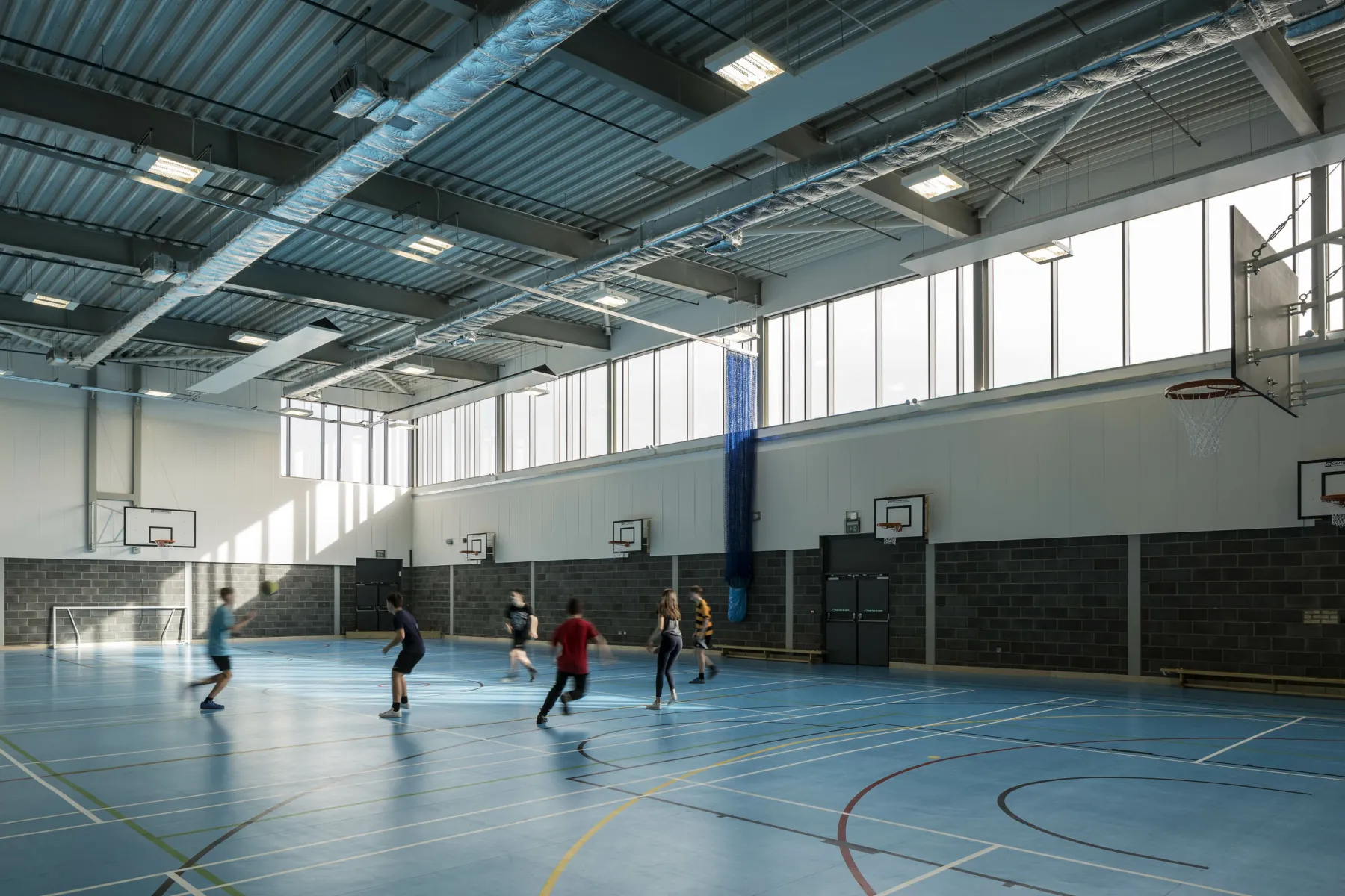 Inside a new build multipurpose games hall at Garnock School, Scotland. A group of pupils play footbal. The floor is marked for different sports including football and basketball.
