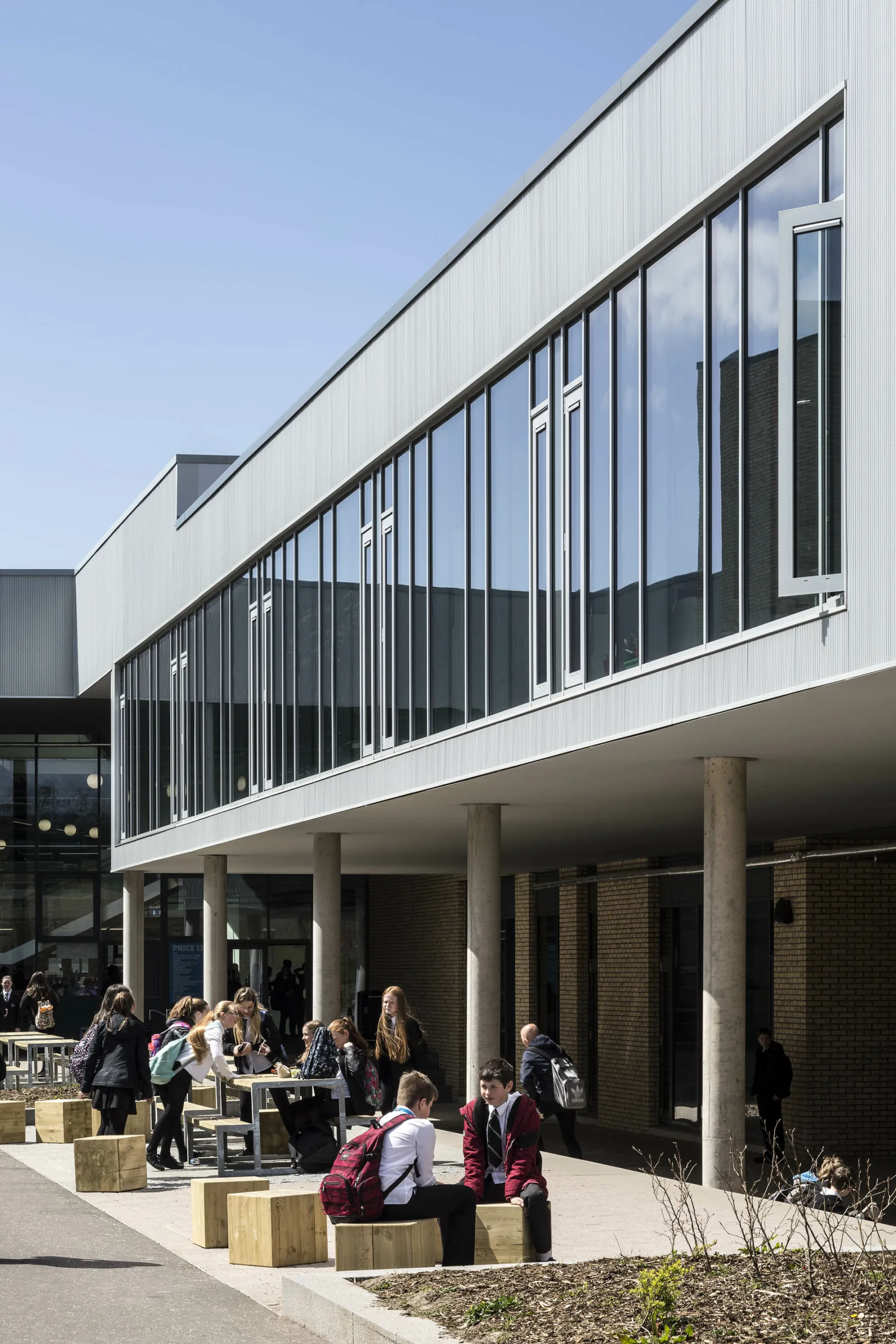 The exterior of the new build Garnock School showing pupils having lunch at benches and tables in the sunshine