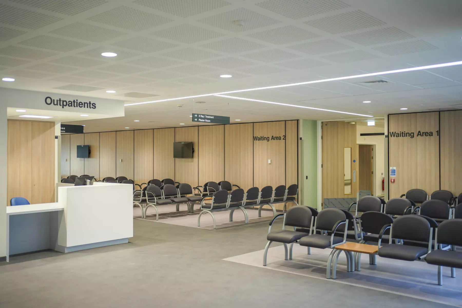 Waiting room with black chairs in the National Treatment Centre - Fife Orthopaedics. Wood clad walls and a white ceiling in the brightly lit space.