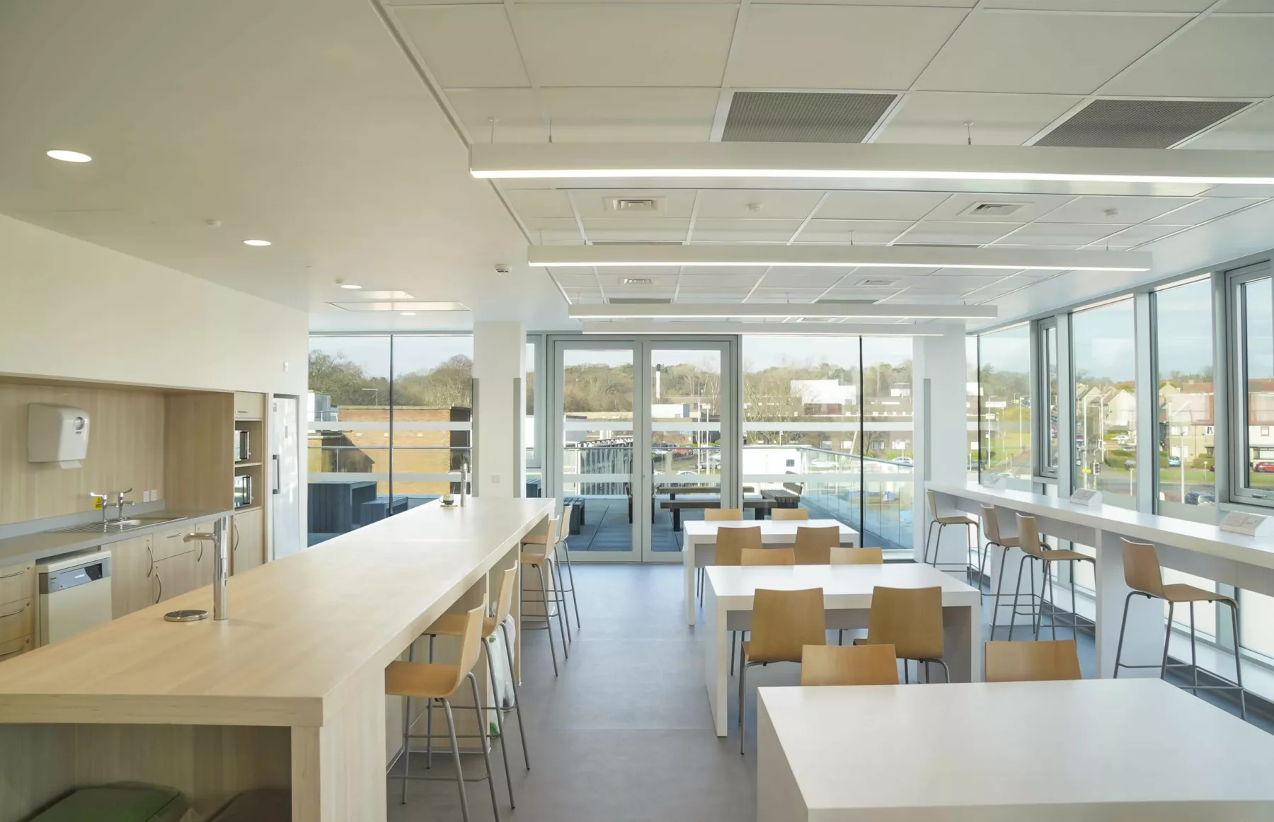 Staff kitchen and eating area at the National Treatment Centre - Fife Orthopaedics. Large windows on two sides, tables and chairs at varying heights in the bright and clean space.