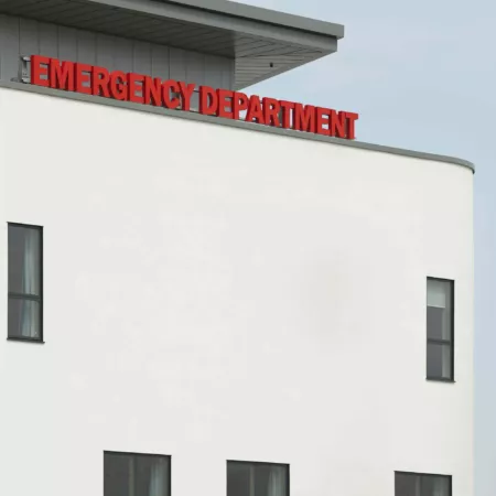 Exterior detail of the Emergency Department of the Royal Hospital for Sick Children and Young People, Edinburgh. A large, illuminated red sign "Emergency Department" sits above the main entrance to the white-rendered building.
