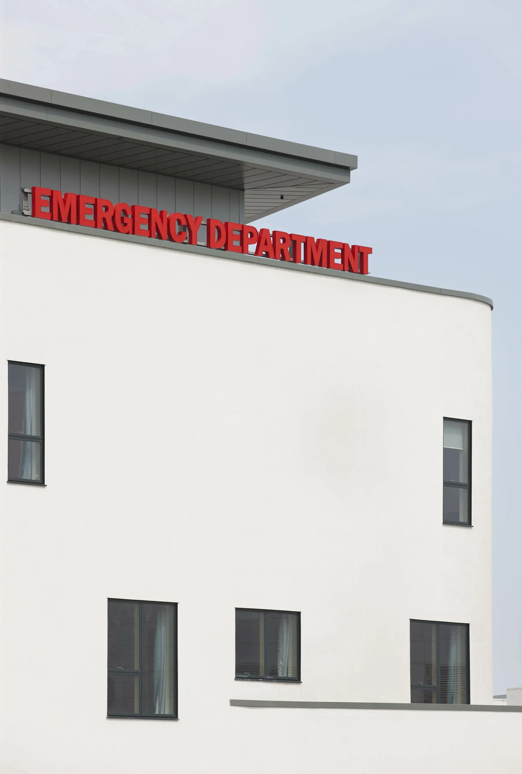 Exterior detail of the Emergency Department of the Royal Hospital for Sick Children and Young People, Edinburgh. A large, illuminated red sign "Emergency Department" sits above the main entrance to the white-rendered building.