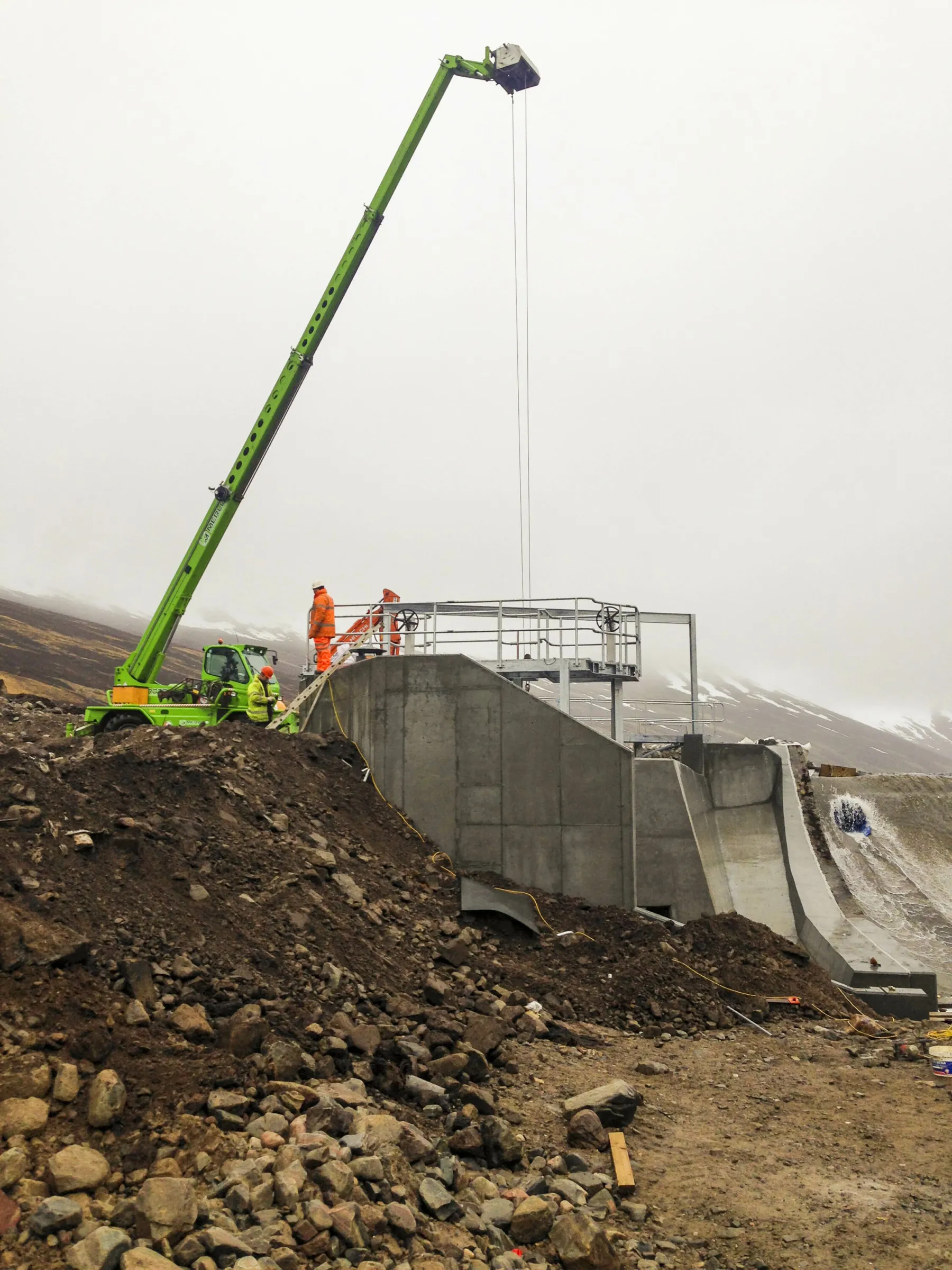 Construction consultants visiting the site of a hydro project in Scotland. A crane is positioned behind the site of a new hydro structure made in concrete.