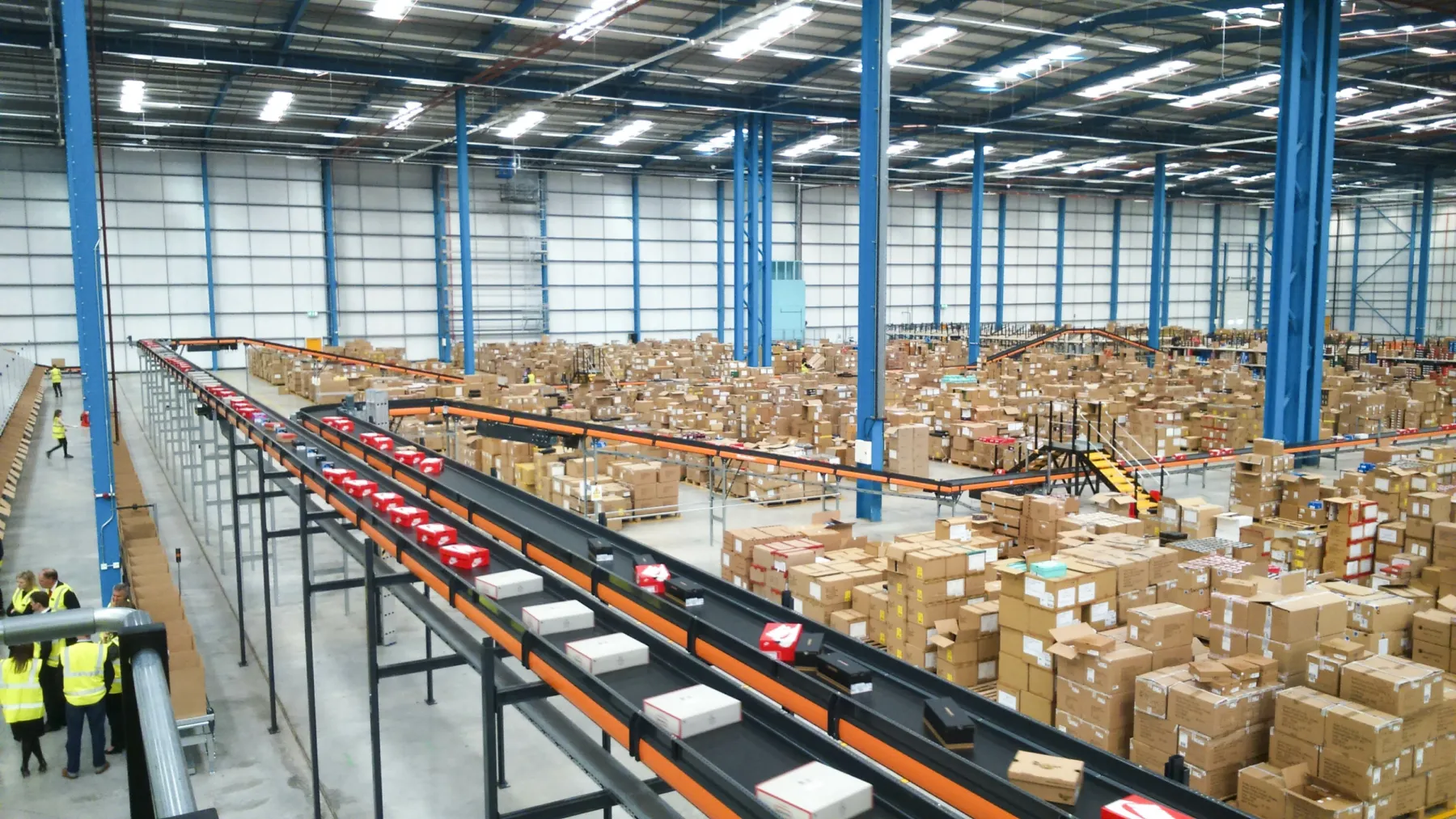 Inside the schuh distribution warehouse, a newly built facility. Conveyer belts at high level move boxes of shoes, with stock stacked in large boxes throughout the warehouse