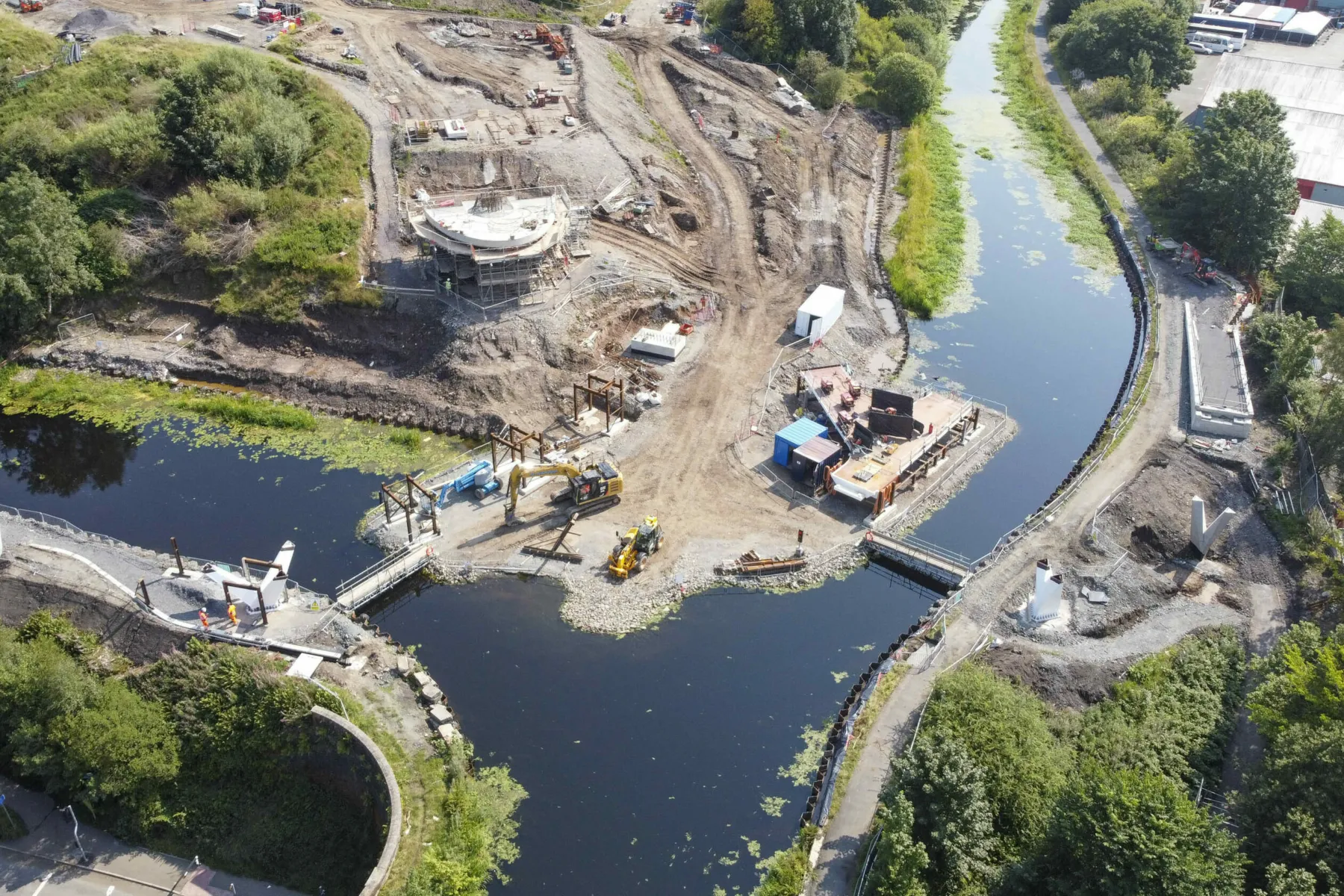 Construction site during the building of Stockingfield Bridge, Glasgow. Temporary causeways over two sections of canal at the forked junction of two sections of the Forth and Clyde Canal. The site is shown in summer with earth works underway and the early stages of the bridge tower in progress.