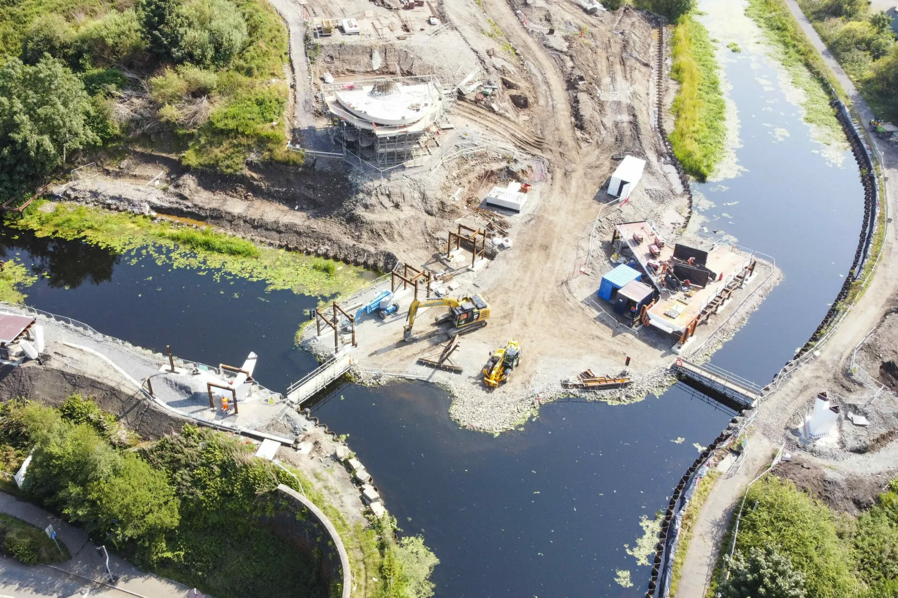 Canal bridge under construction at the site of the Stockingfield Bridge, Glasgow. The early stages of the tower are in progress. Gangways are show across two points in the canal to allow access and boats to pass. Earthworks are underway.