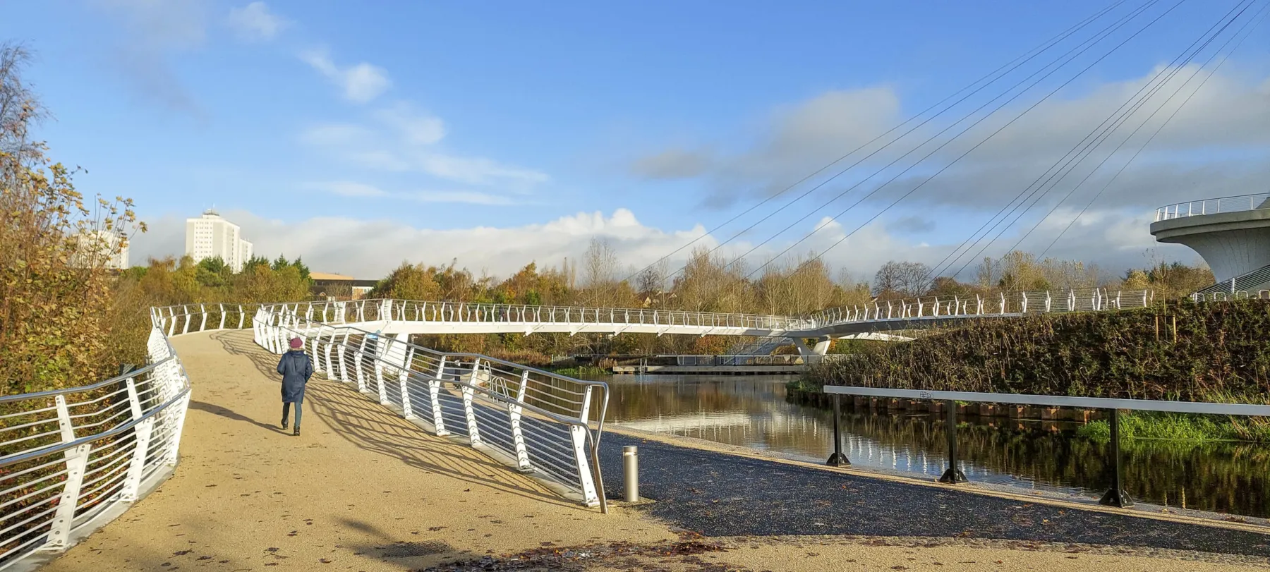 A view of one of the entrances to the Stockingfield Bridge. A wide path suitable for pedestrians, cyclists and those with accessibility needs has a non slip surface and white railings.