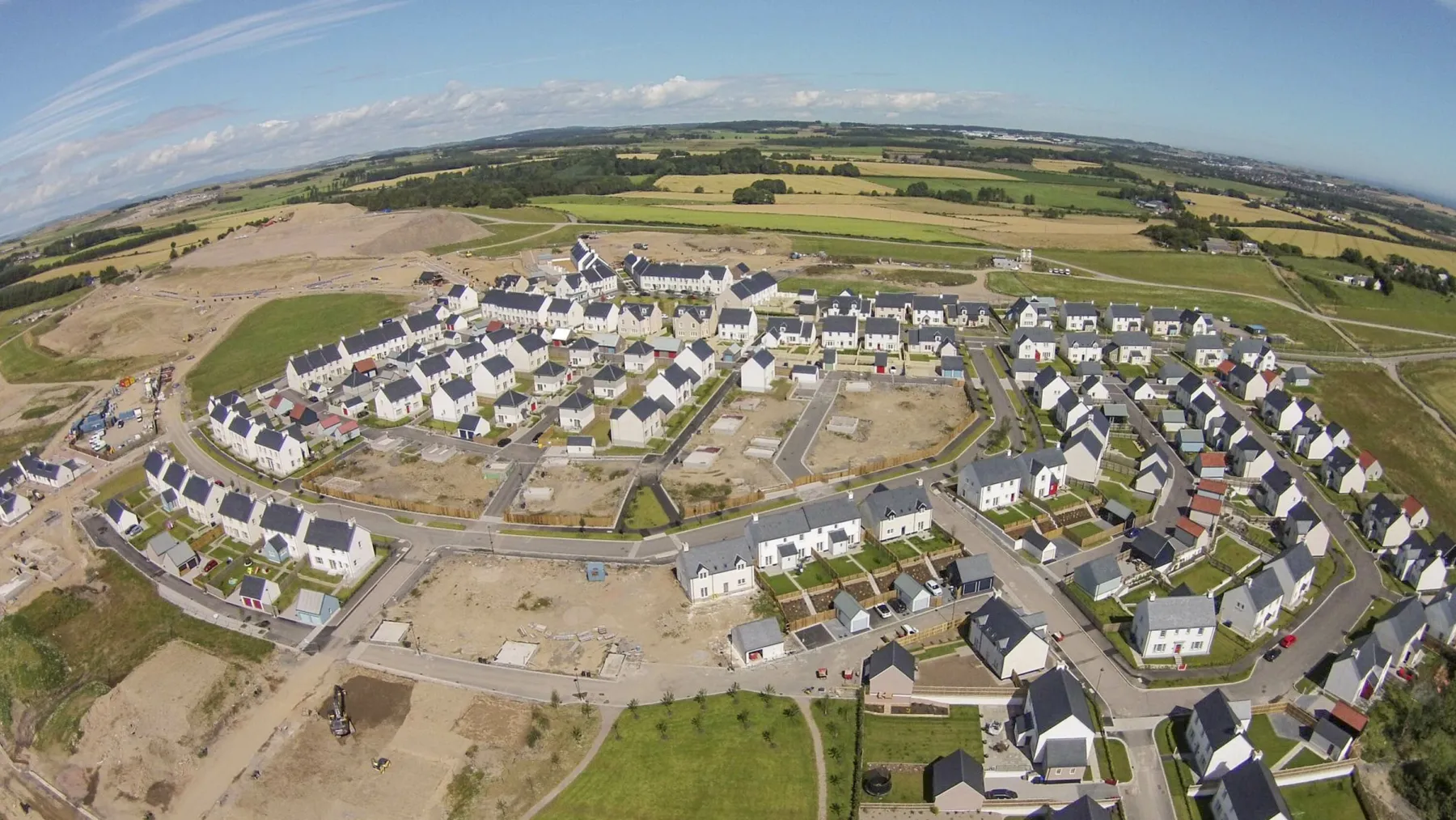 The new village at Chapelton of Elsick seen from the air. Ground works and construction continues at the edge of the photograph. The site is surrounded by farmland and containse several streets in a grid and crescent formation