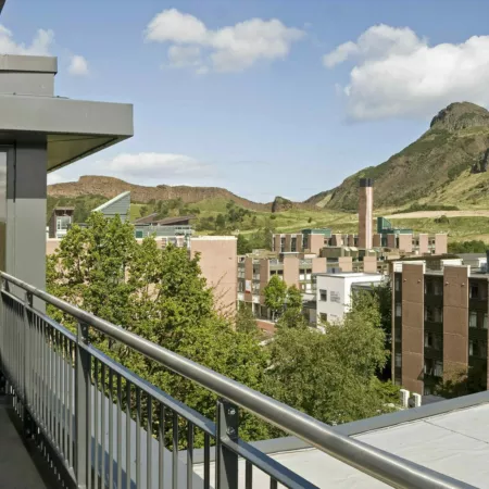 View from top floor balcony at John Burnett House, student accommodation at the University of Edinburgh's Pollock Halls. Beyond further student blocks is a view of Salisbury Crags and Arthur's Seat. It is a sunny day with light clouds,